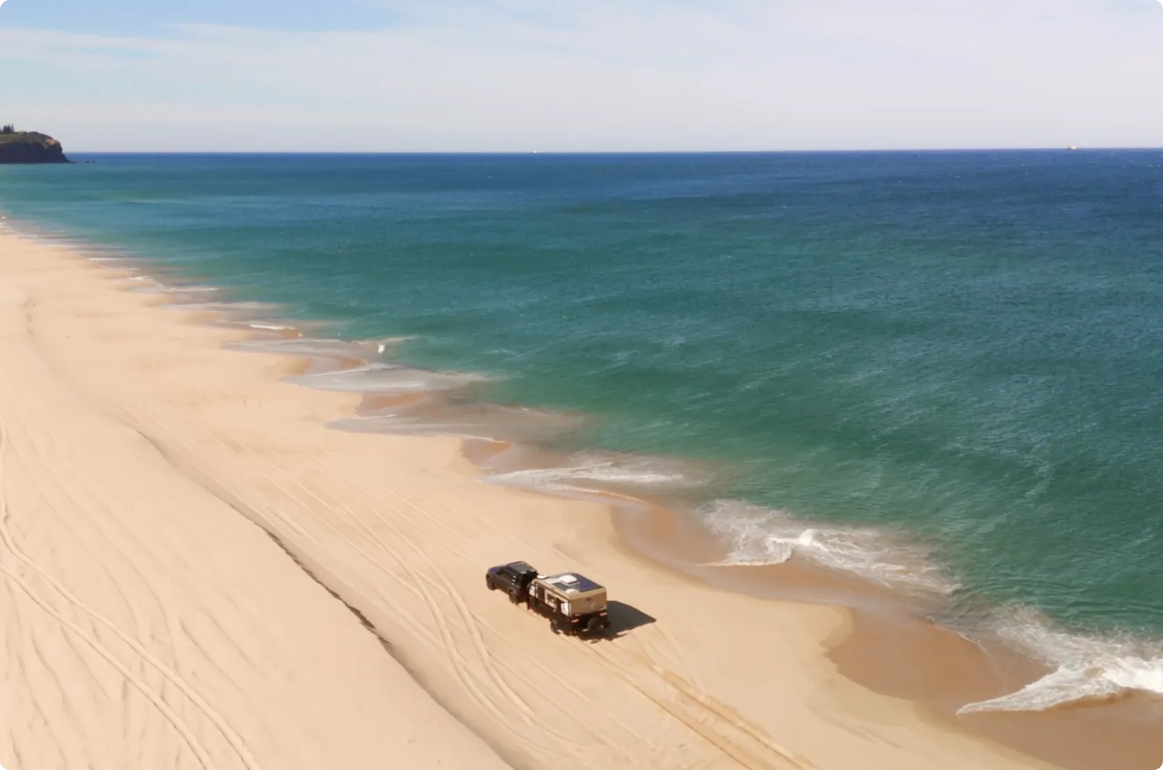 A four-wheel drive towing an off-road camper along an empty Australian beach