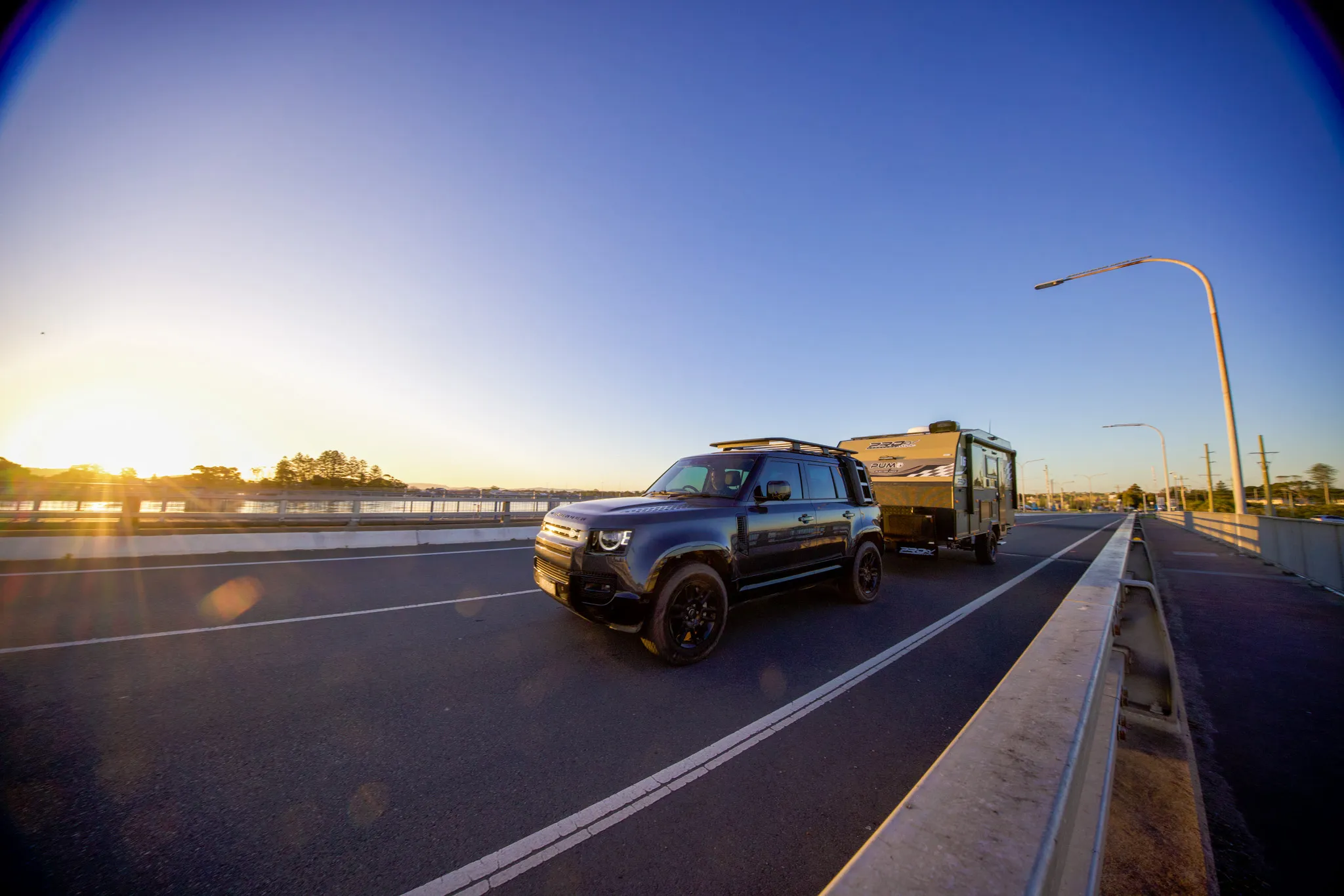 A four-wheel drive towing a caravan along a coastal highway at sunrise