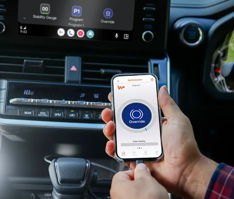 A driver holding a phone running the Elecbrakes App, with Android Auto on the dashboard screen behind