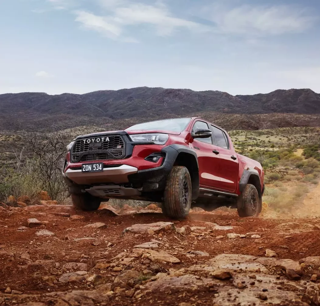 A red Toyota HiLux GR Sport climbing a rocky outback track