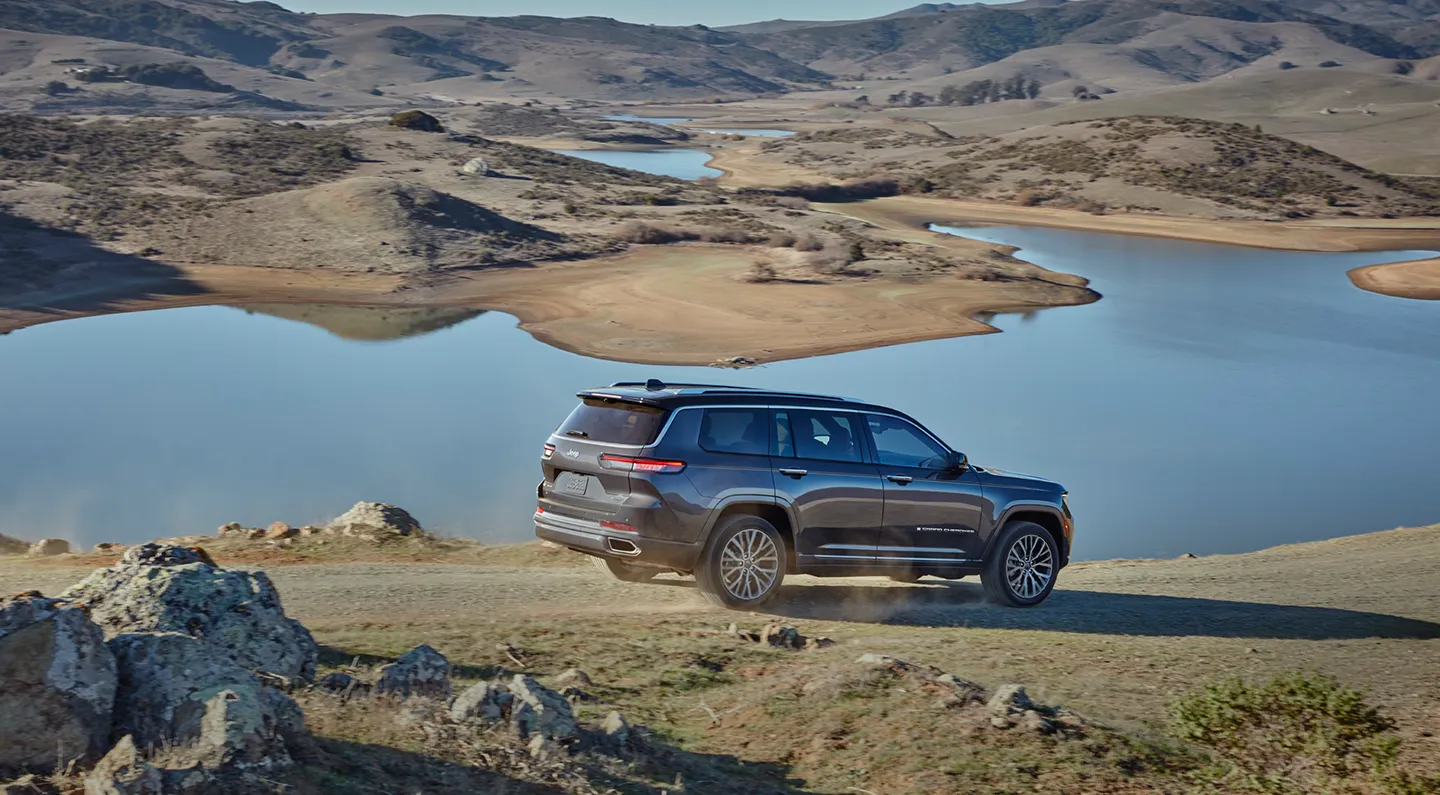 A grey Jeep Grand Cherokee on a gravel ridge above a lake