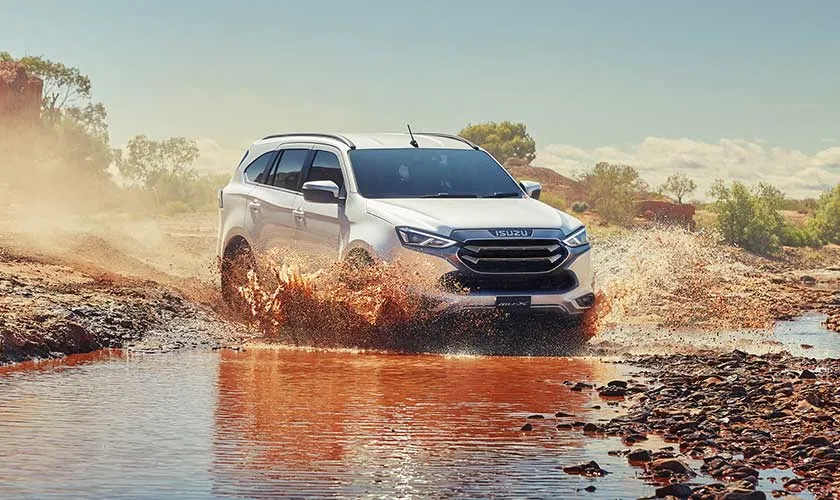 A white Isuzu MU-X driving through a shallow outback river crossing