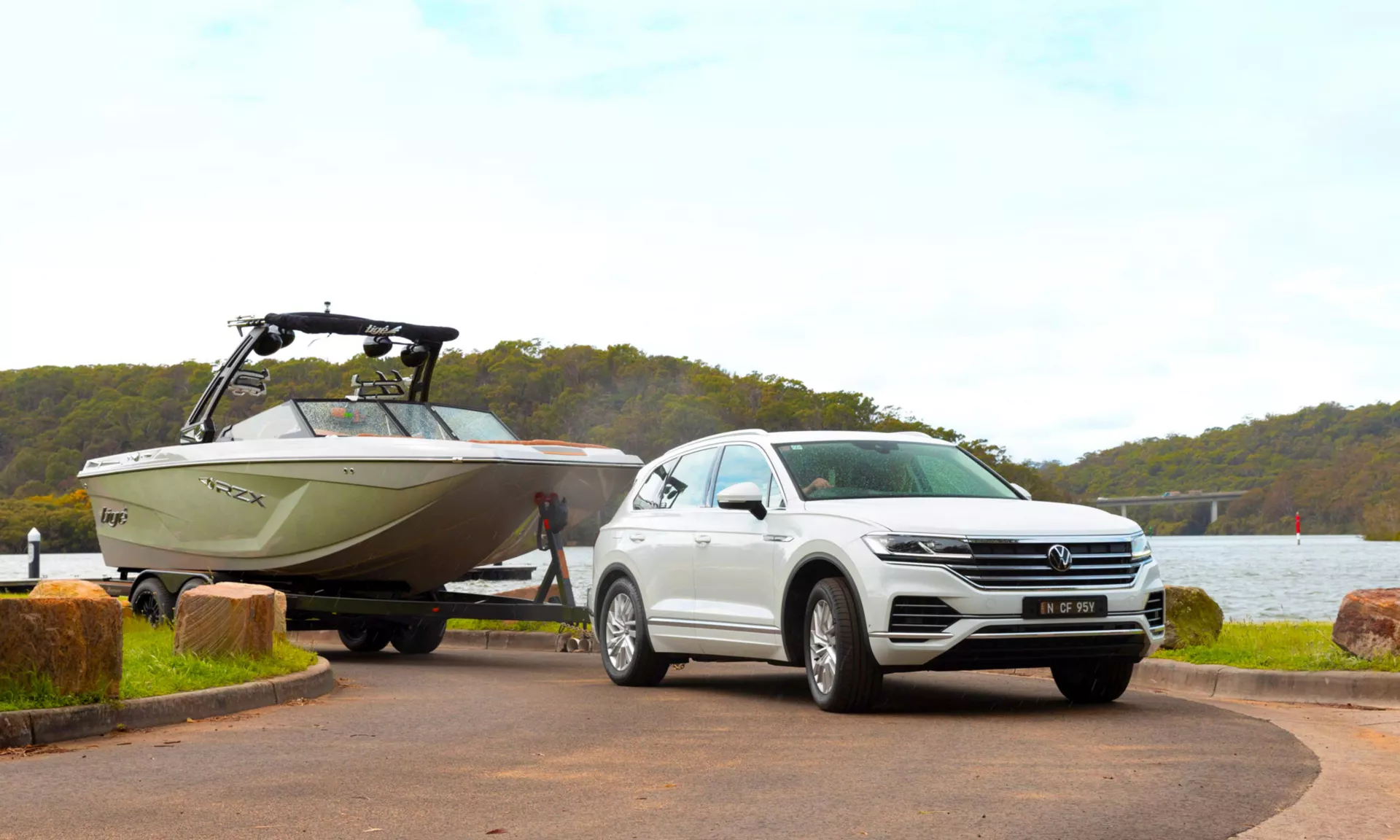 A white Volkswagen Touareg towing a ski boat on a trailer beside a lake