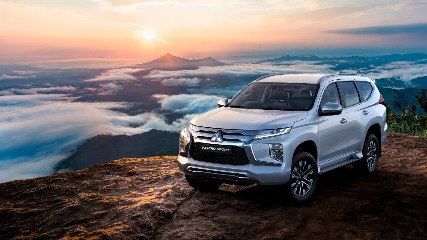 A silver Mitsubishi Pajero Sport parked on a clifftop above the clouds