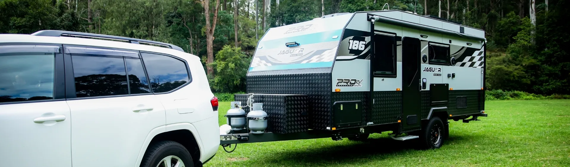 White SUV towing a JAGU-R caravan on green grass with trees in the background.