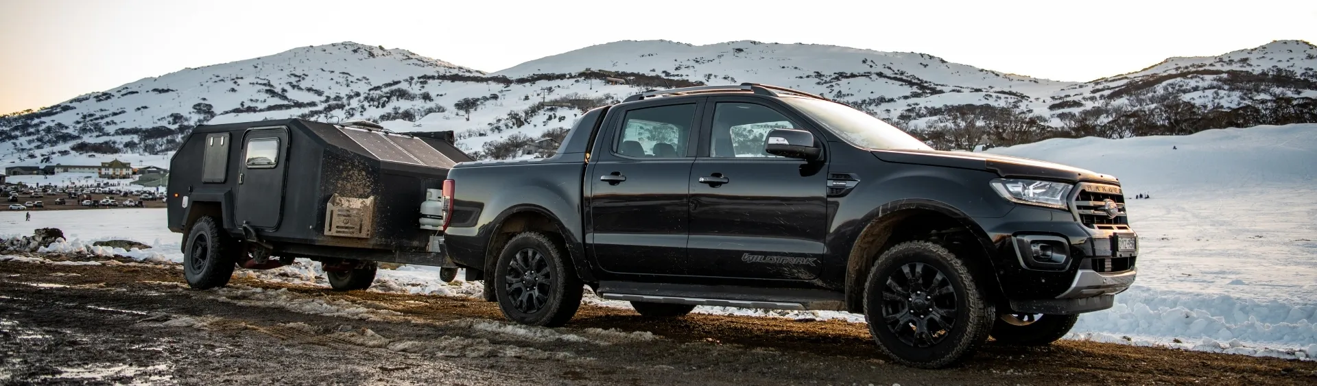 Black Ford Ranger towing trailer in snowy landscape.