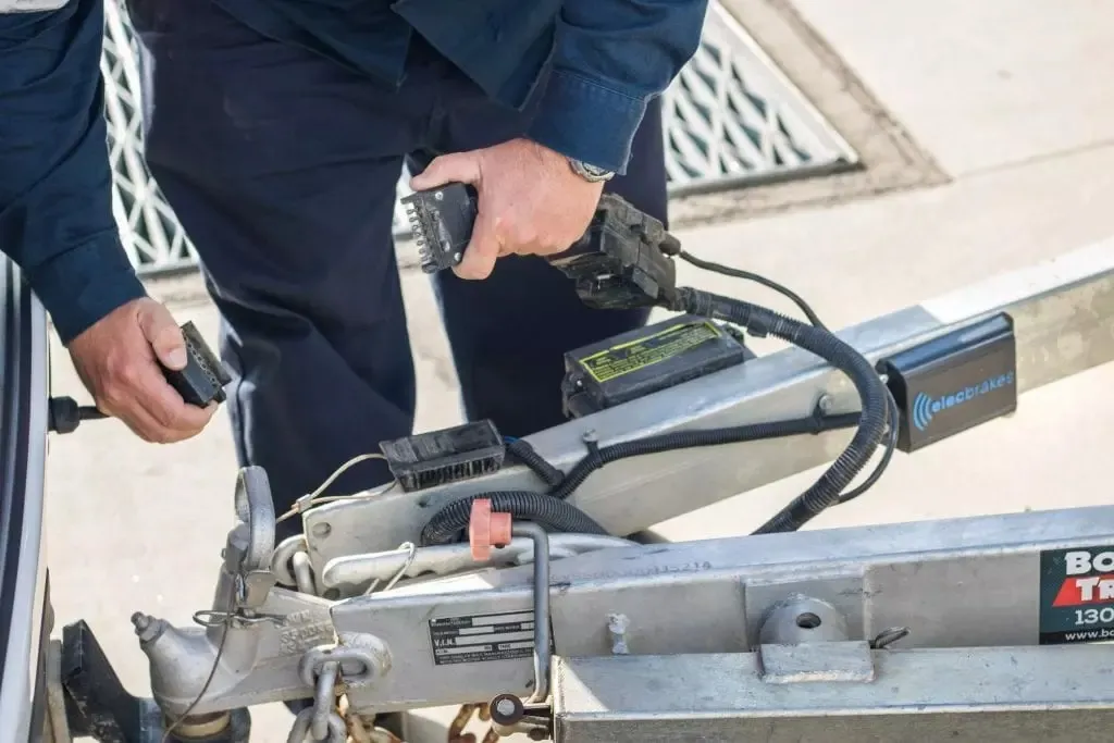 A technician connecting trailer plugs beside an Elecbrakes controller on a trailer drawbar
