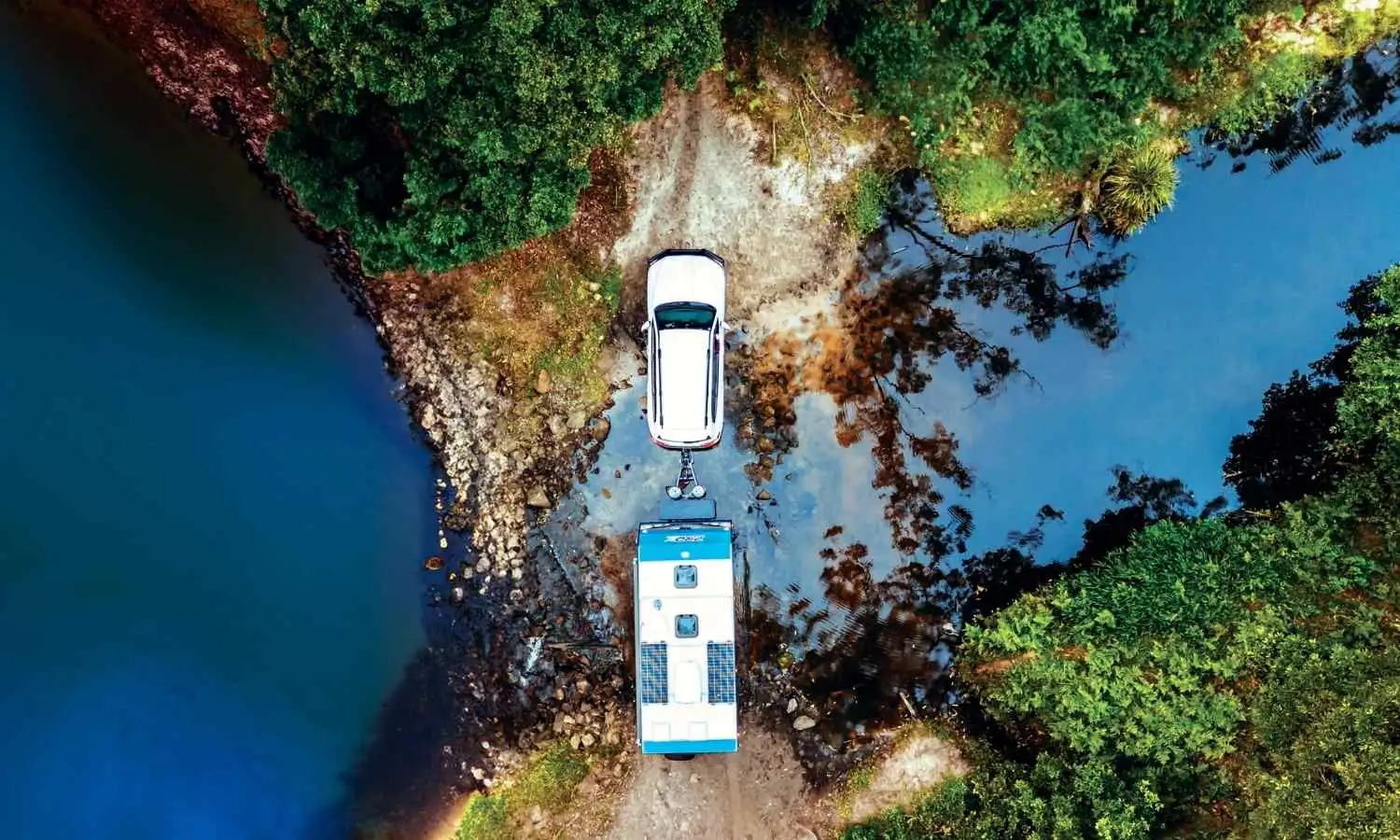 Aerial view of a caravan being towed through a clear creek surrounded by bushland