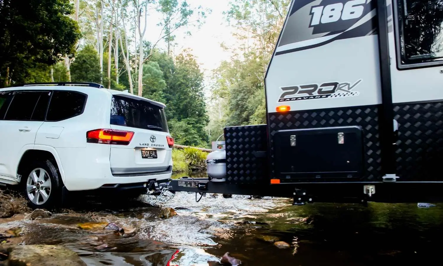 4WD towing a caravan through a shallow creek crossing on an off-road track