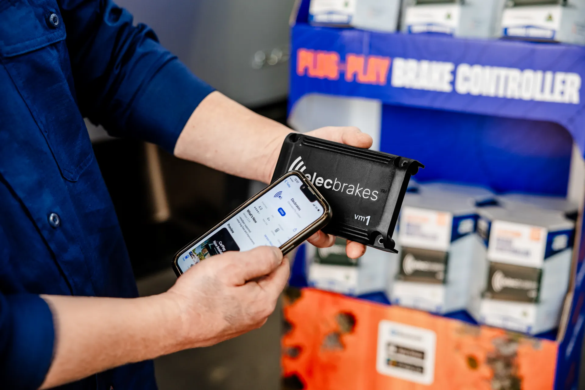 An Elecbrakes staff member holding a VM1 alongside a phone showing the Elecbrakes App listing