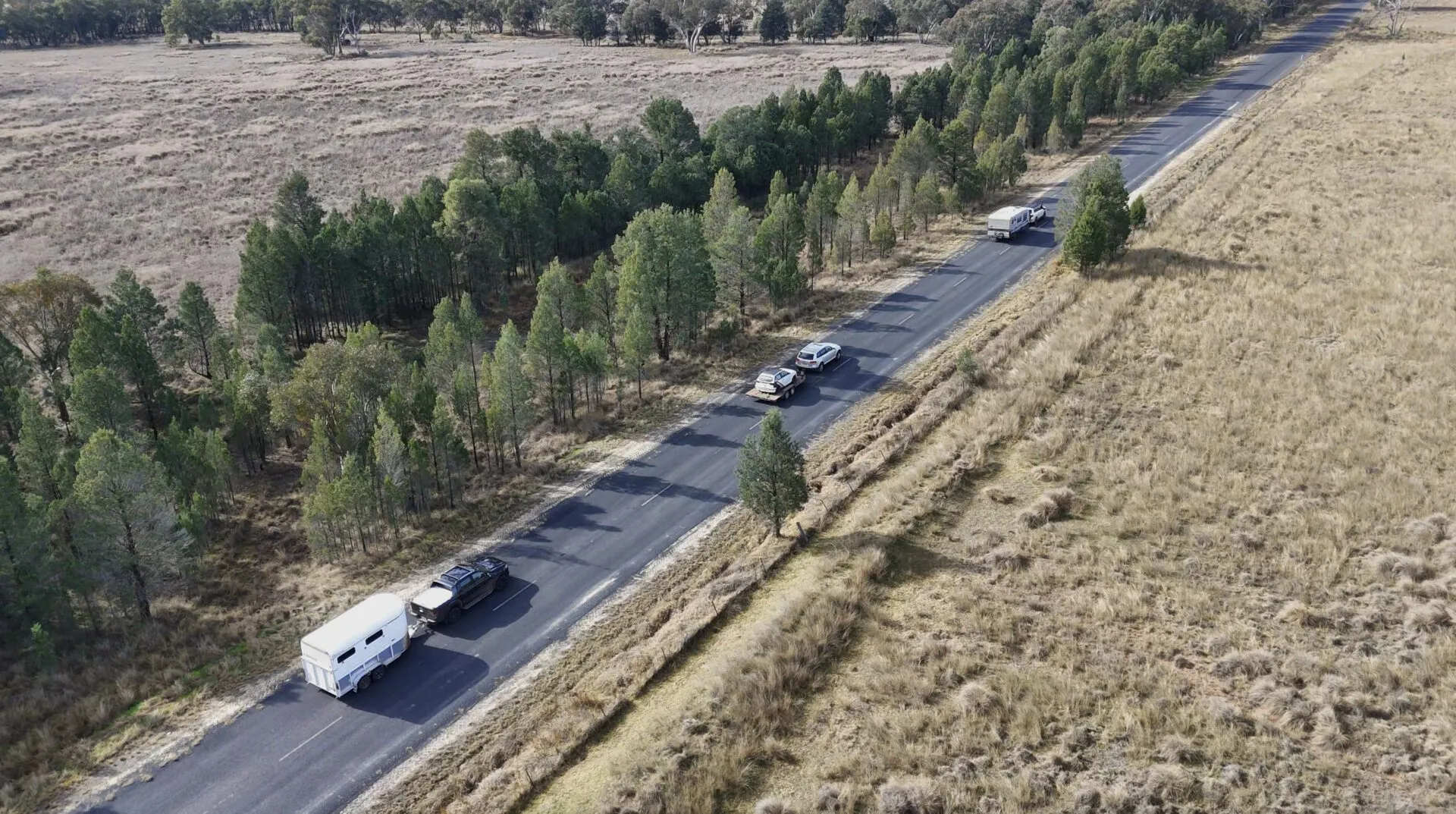 An aerial view of vehicles towing a horse float, a car trailer and a caravan along a country road