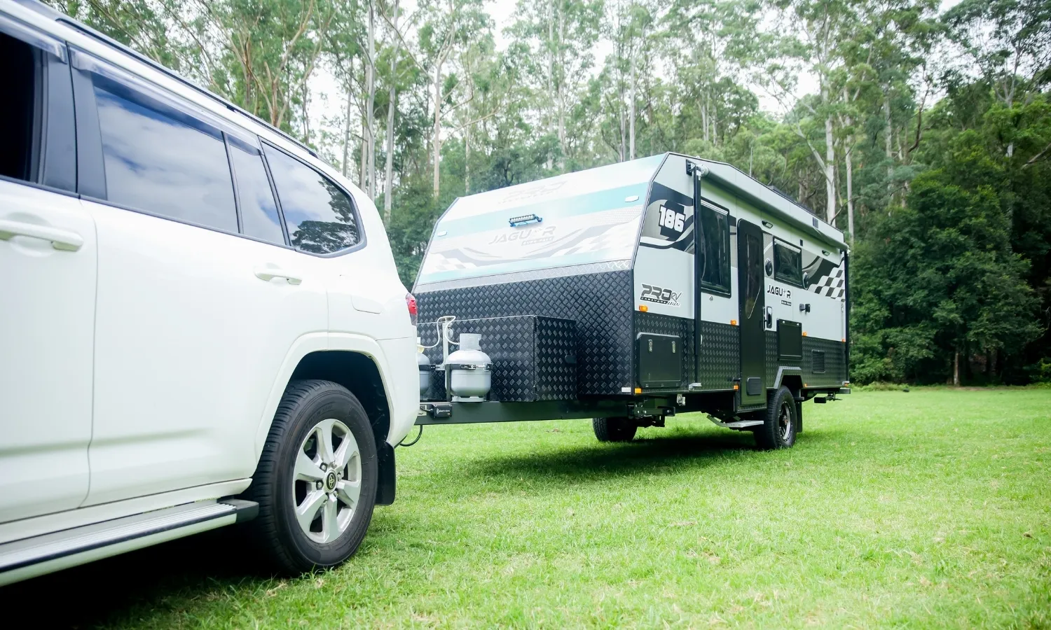 White SUV towing a white caravan on grass in an open outdoor area