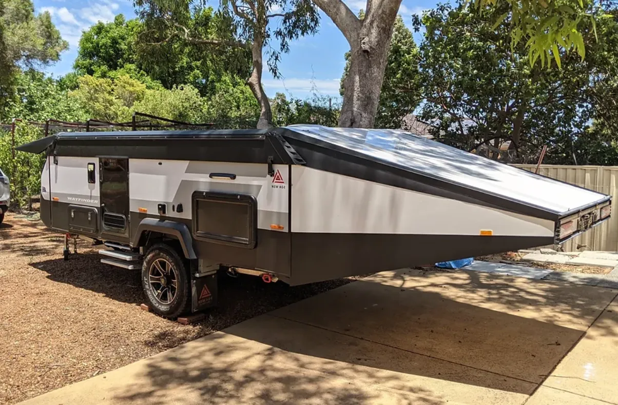 A New Age Wayfinder camper set up with its roof extended on a driveway