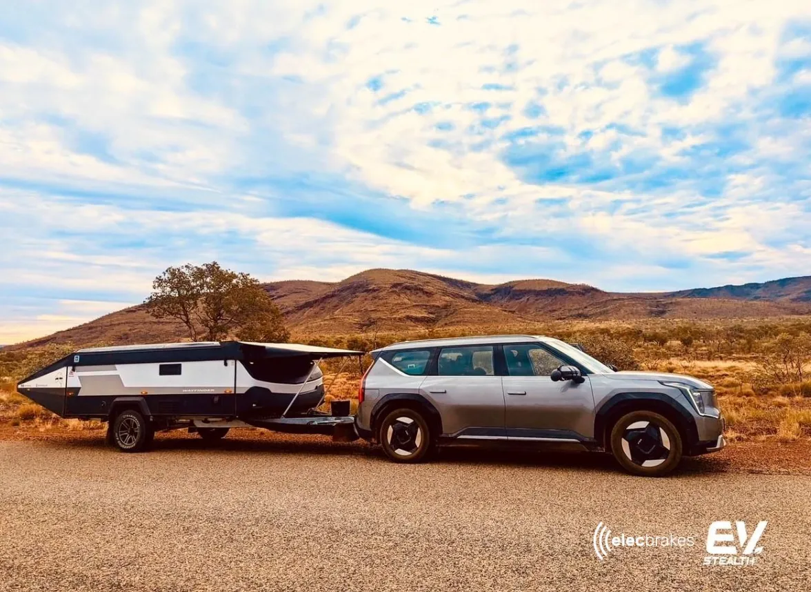 A Kia EV9 towing a New Age Wayfinder camper on an outback road