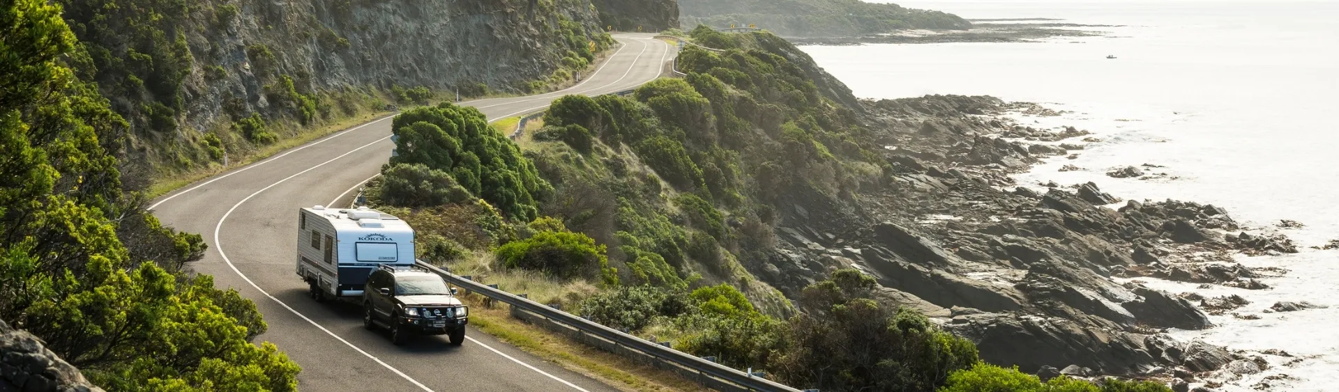 Car and caravan towing along the Great Ocean Road with sweeping coastal views and cliffs