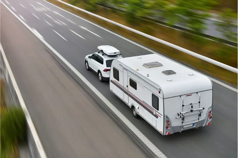 A car towing a white caravan along a divided highway, seen from above