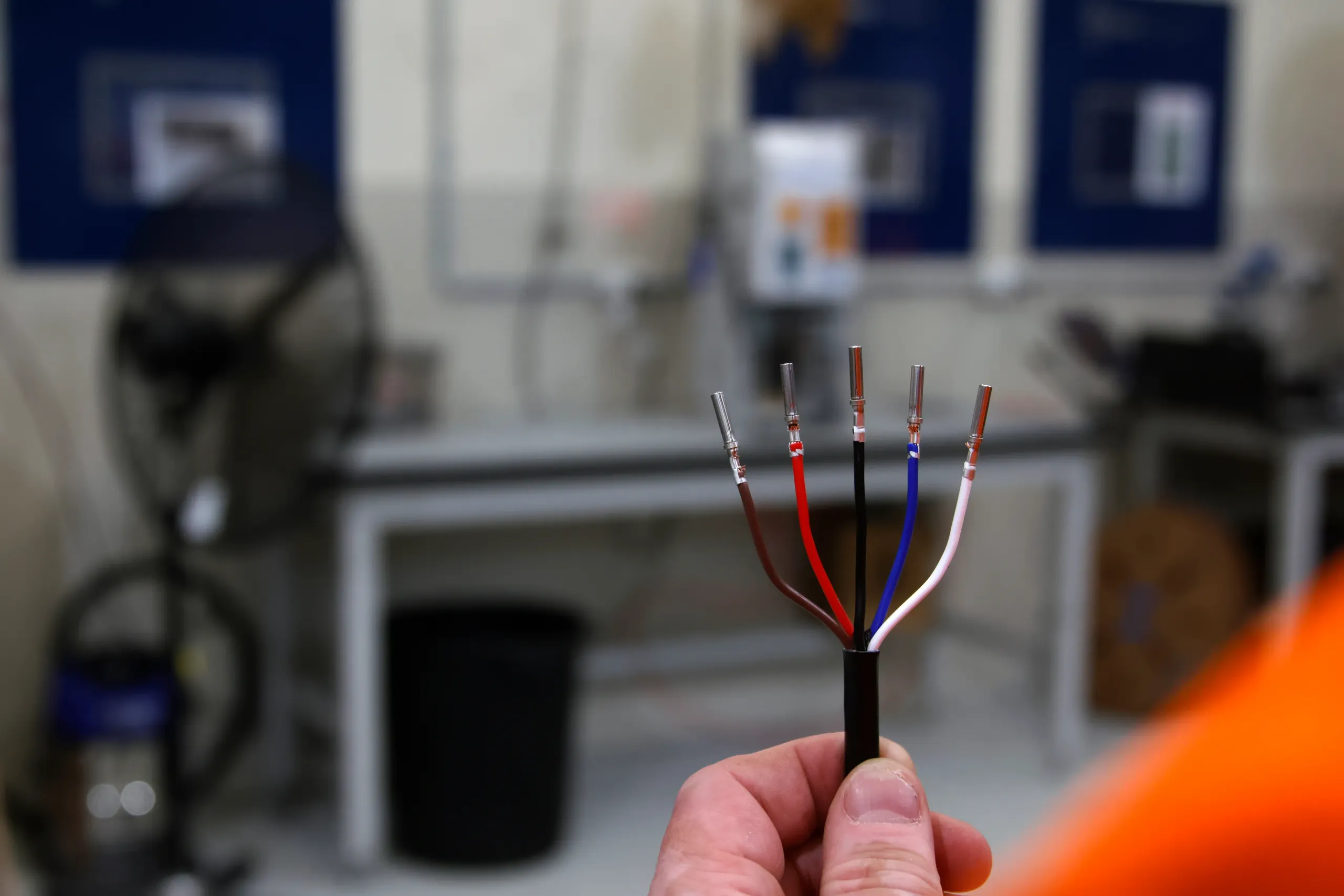 The bare end of an Elecbrakes Wired Leader held up in a workshop, its five cores fanned out in brown, red, black, blue and white with crimped pins fitted